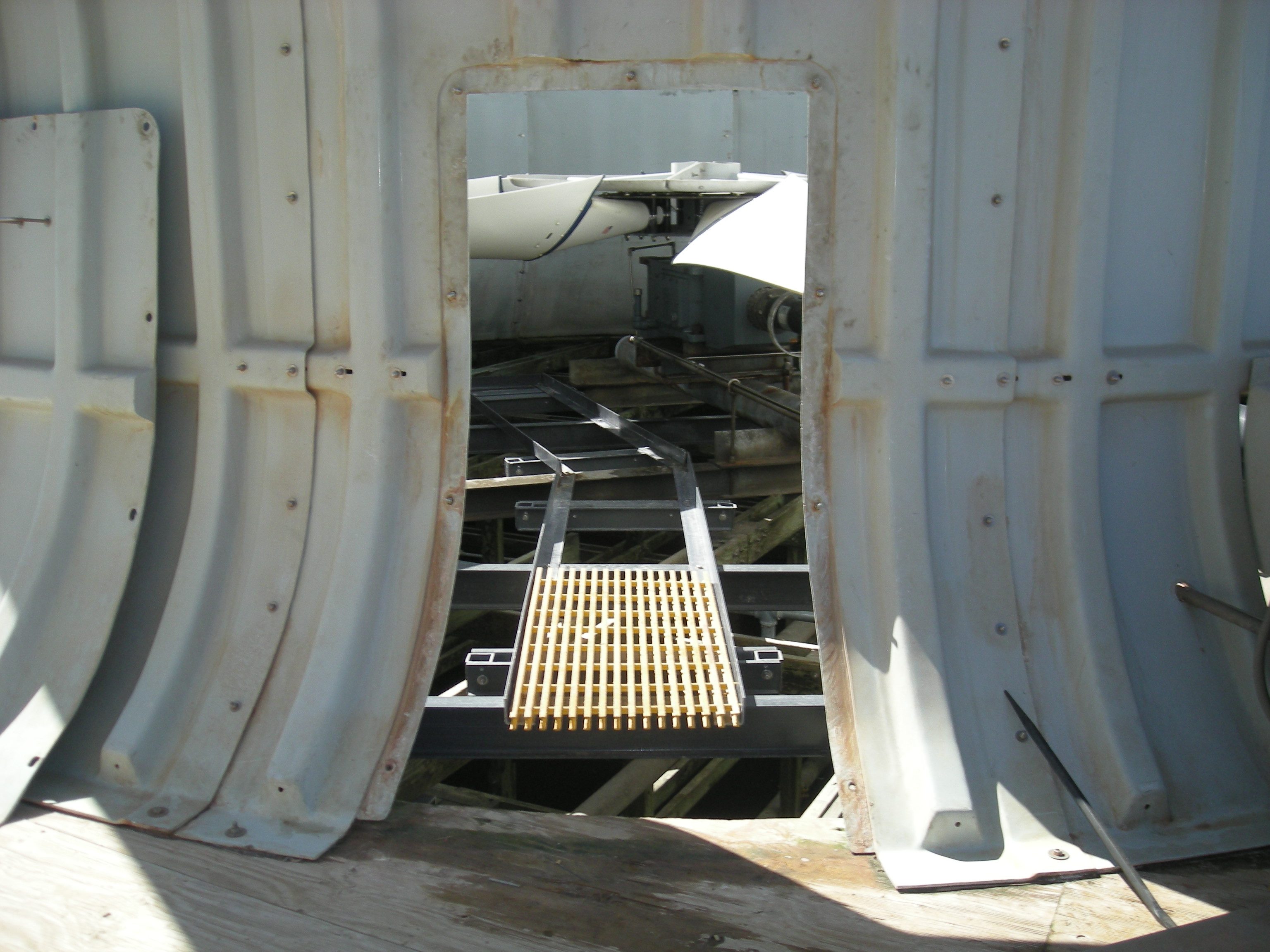 Newly installed bright yellow fiberglass grating on a black steel walkway frame inside a cooling tower, seen through an access door in the casing.