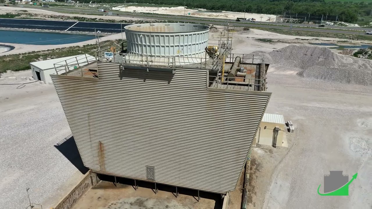 Aerial view of a field-erected cooling tower with corrugated casing, a round fan stack on the deck, process ponds to the left and a highway in the distance.